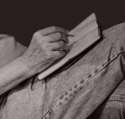 black and white image of an person writing in a note book which is leaning on their legs
